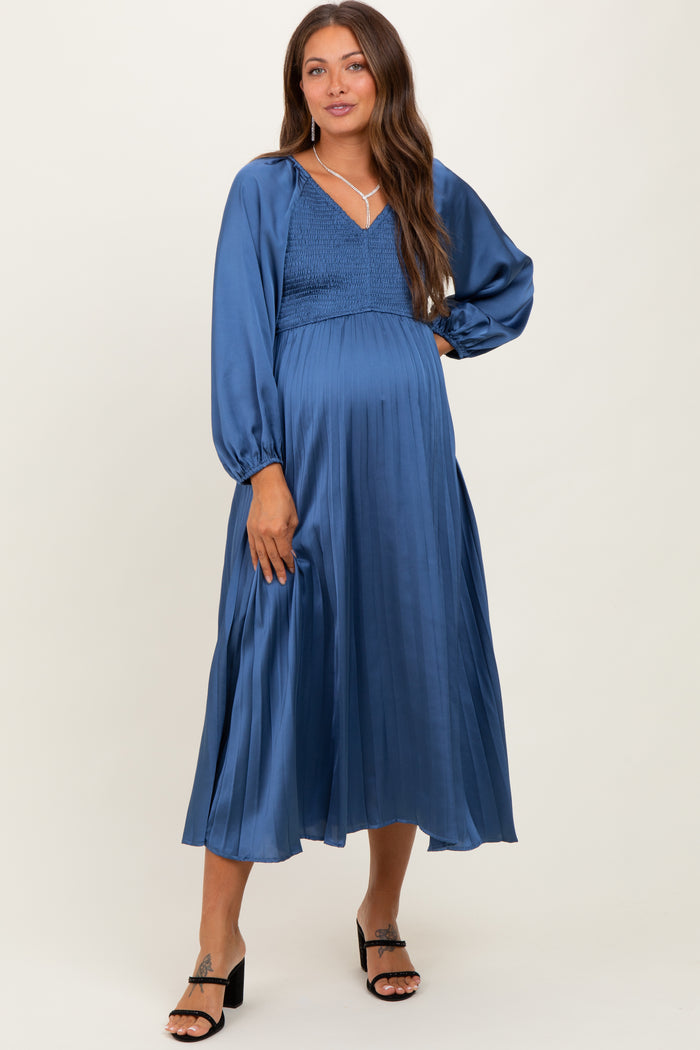 woman wearing a satin blue maternity dress with a smocked bodice and long puff sleeves, showcasing her baby bump