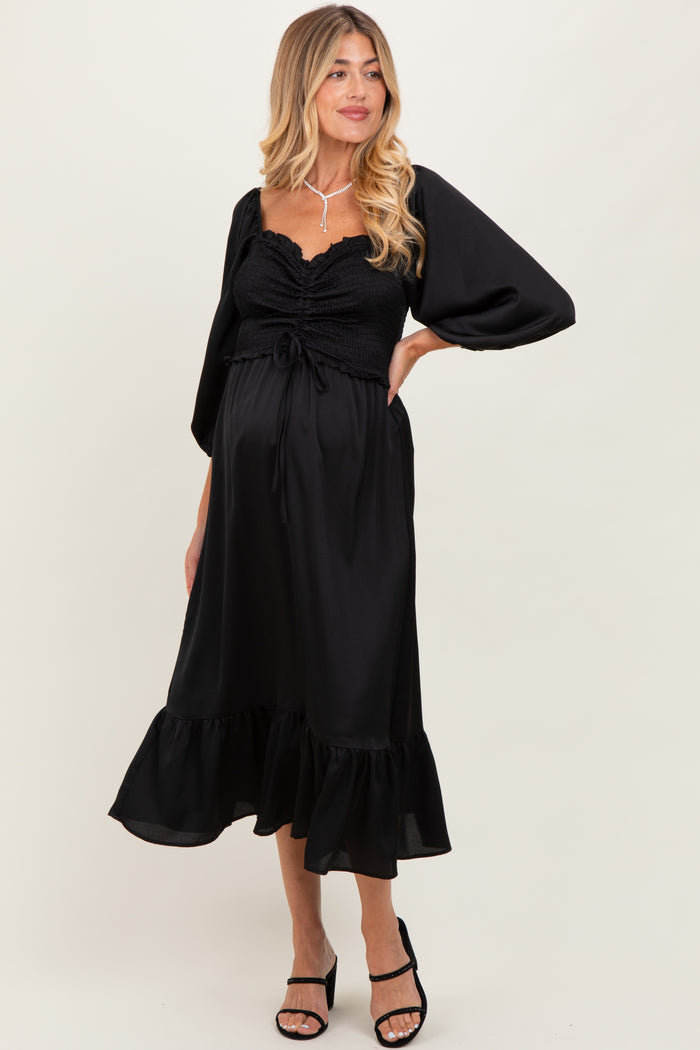 woman wearing a black maternity dress with puff sleeves and ruffle hem, showing her baby bump