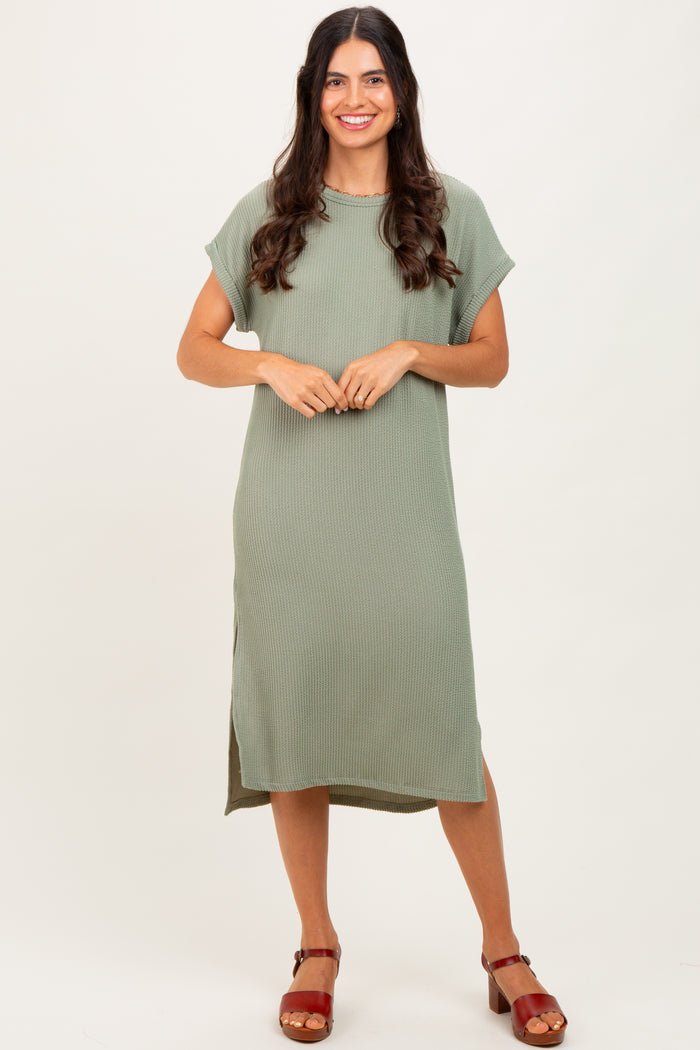 woman wearing a sage green ribbed midi dress with short sleeves and side slits, standing on a neutral background