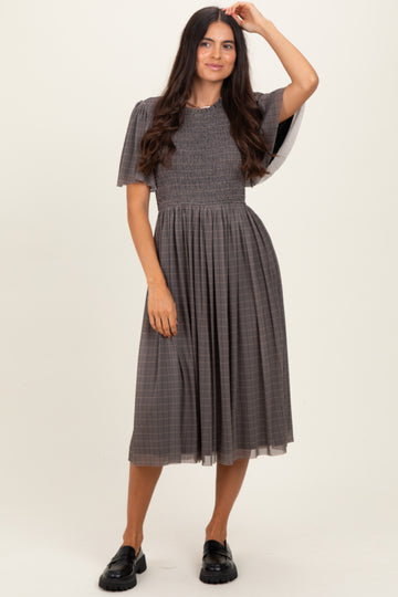 woman wearing a grey plaid midi dress with smocked bodice and puff sleeves, styled with black chunky loafers