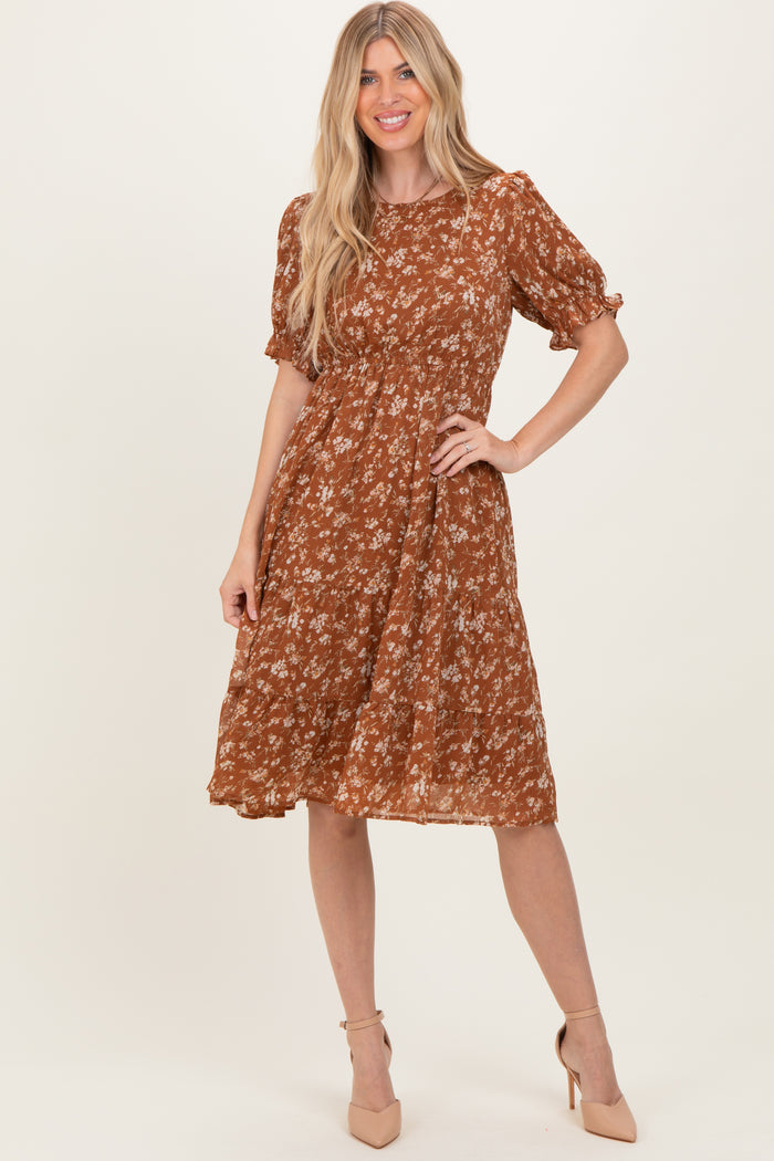 woman wearing a rust floral midi dress with short puff sleeves and a tiered skirt, standing in a playful pose