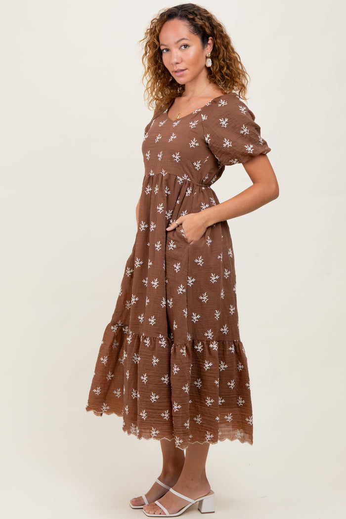 woman wearing a brown floral maxi dress with puff sleeves and pockets, standing sideways against a neutral background
