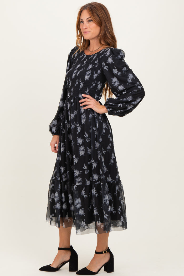 woman wearing a black floral midi dress with puff sleeves and a tiered skirt, styled with black ankle strap heels