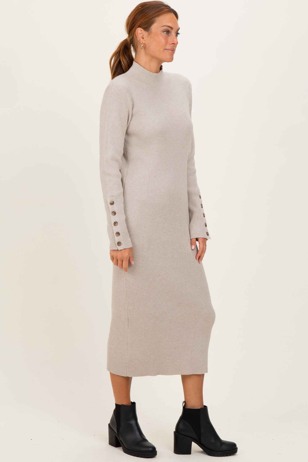 woman wearing a beige ribbed knit long sleeve dress with button details on the sleeves and black ankle boots