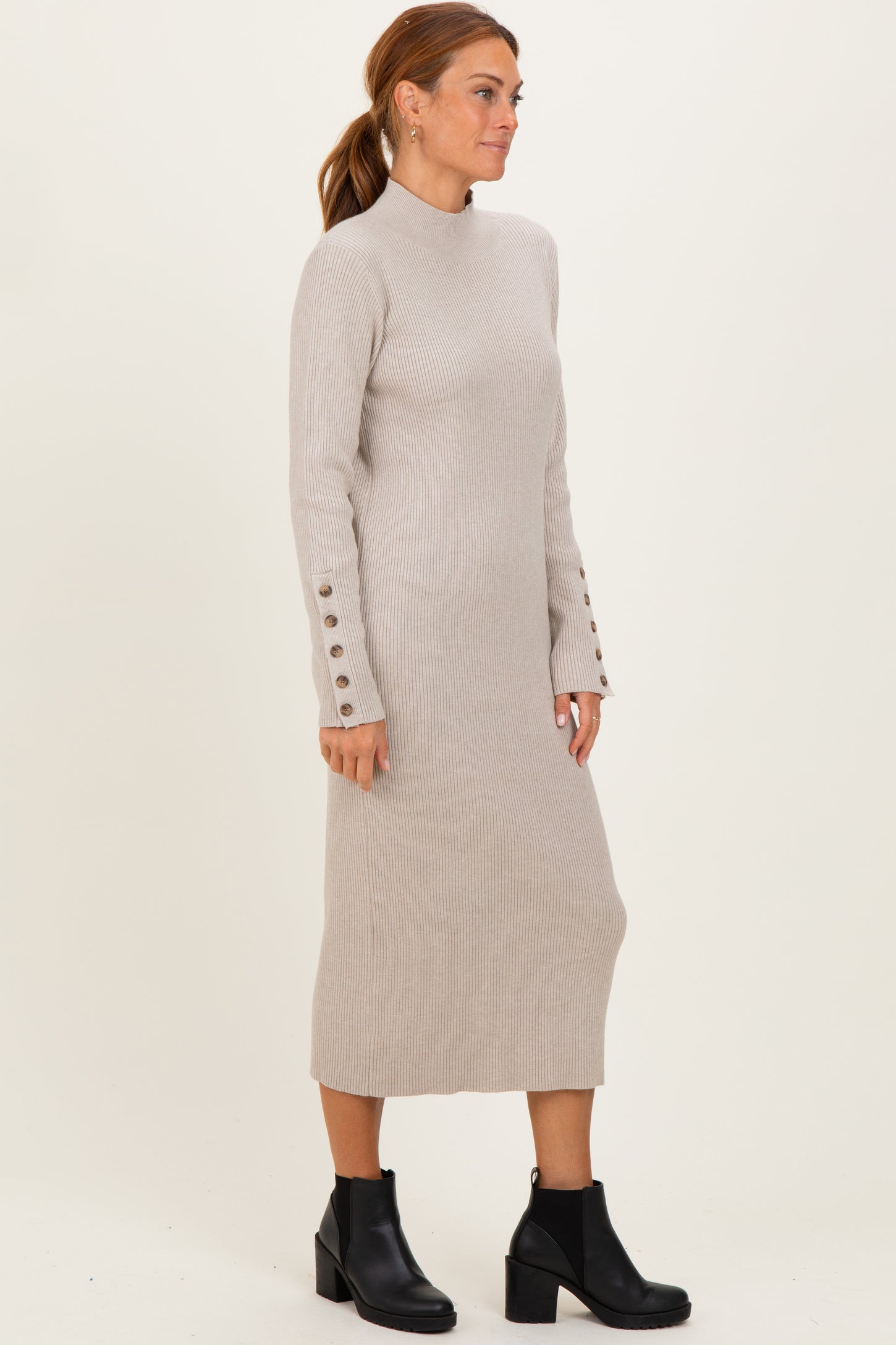 woman wearing a beige ribbed knit long sleeve dress with button details on the sleeves and black ankle boots