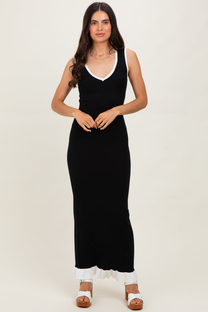 woman wearing a black maxi dress with a white trim and a v-neckline, standing with hands clasped in front