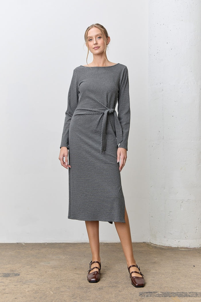 woman wearing a gray striped long sleeve dress with a Tie waist detail, standing against a white wall
