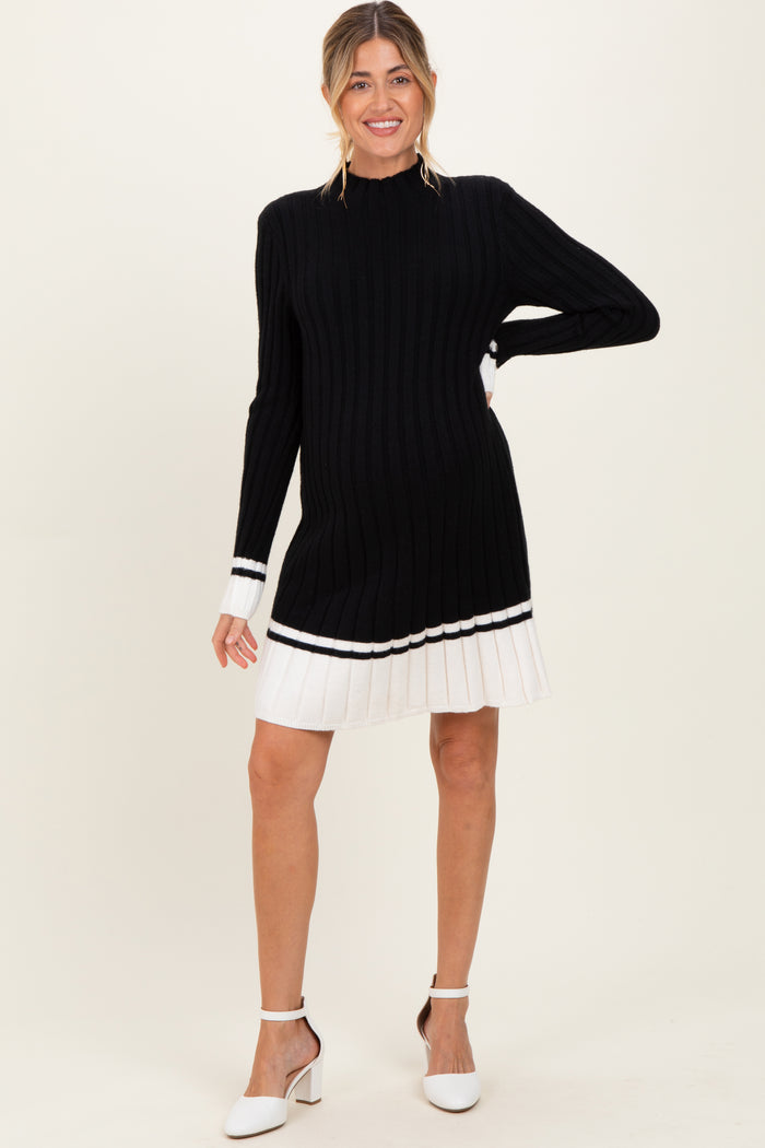 woman wearing a black ribbed maternity sweater dress with white pleated hem and holding her baby bump