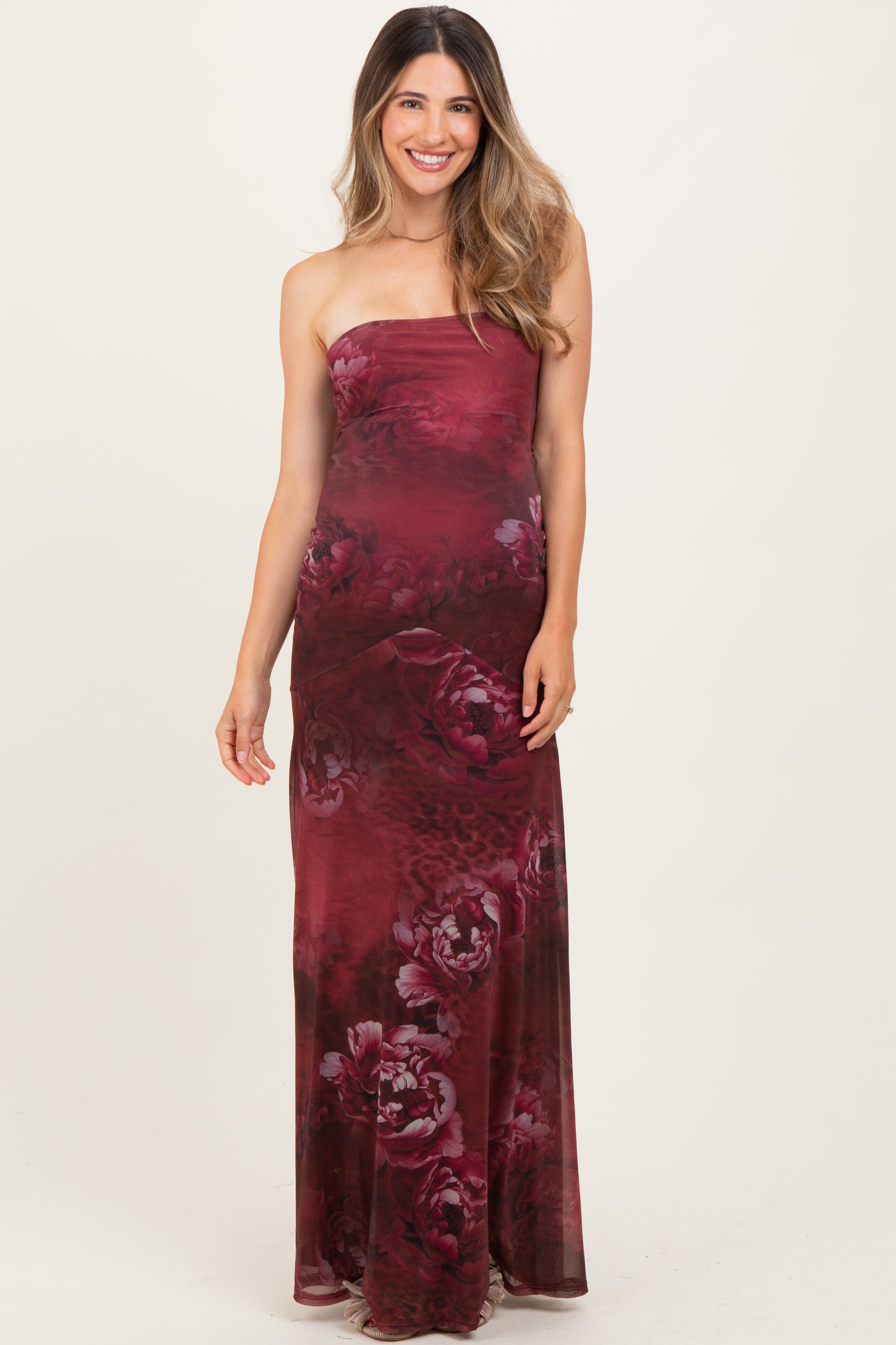 woman wearing a burgundy strapless maternity maxi dress with a floral pattern and a visible baby bump