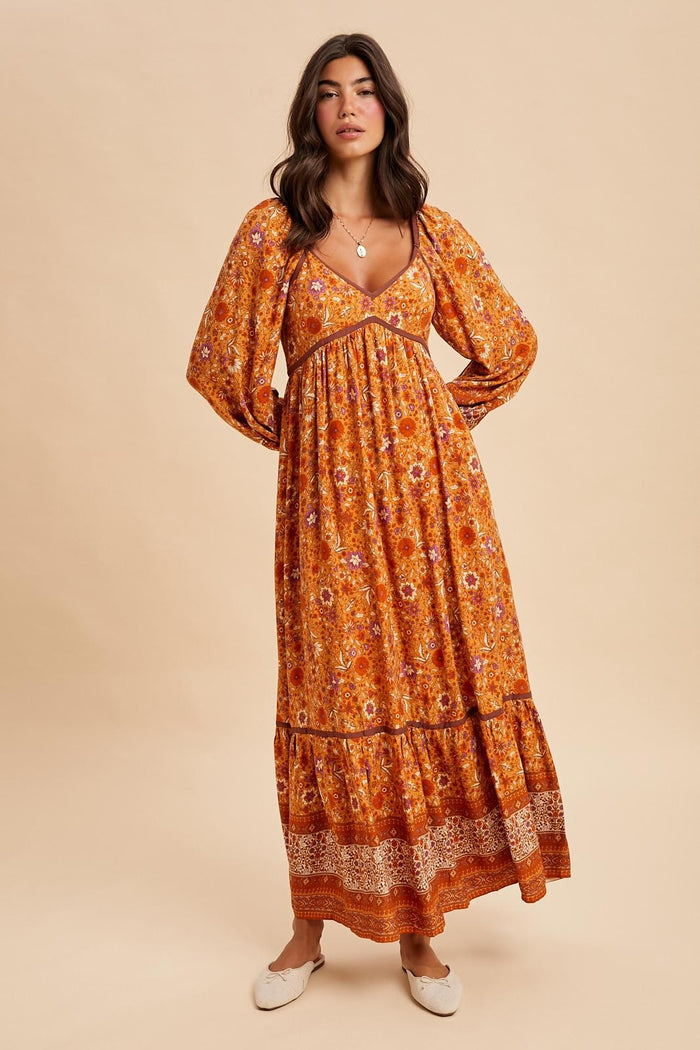 woman wearing an orange floral maxi dress with long sleeves and a tiered hem, styled with a v-neckline