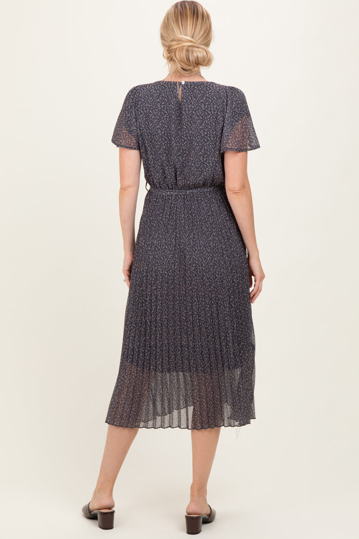 woman wearing a navy blue pleated dress with short sleeves and a cinched waist, viewed from the back