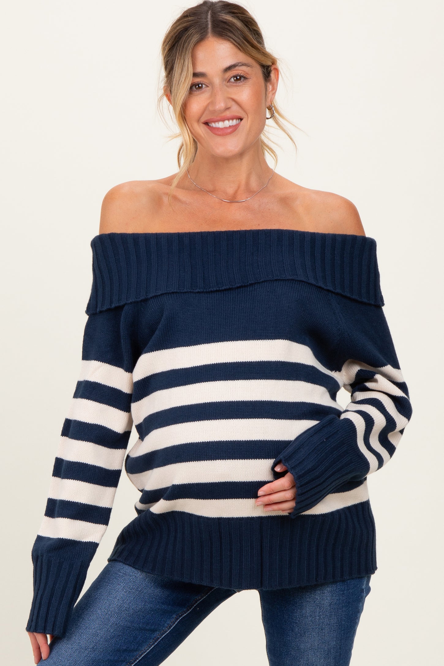 woman wearing a navy and cream striped off-the-shoulder maternity sweater and showing her baby bump