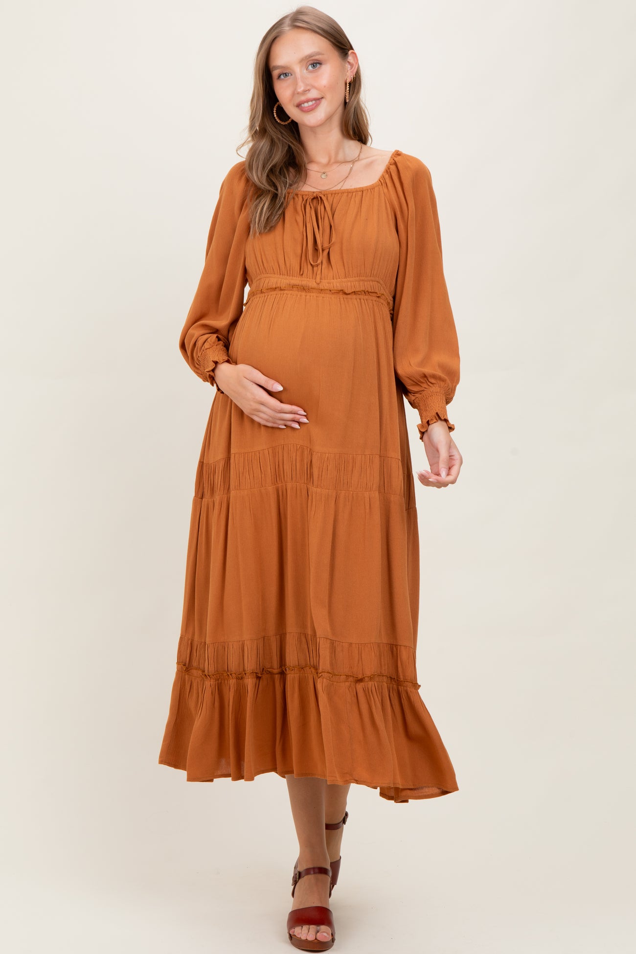 woman wearing a rust-colored long sleeve maternity dress with a tiered skirt and holding her baby bump