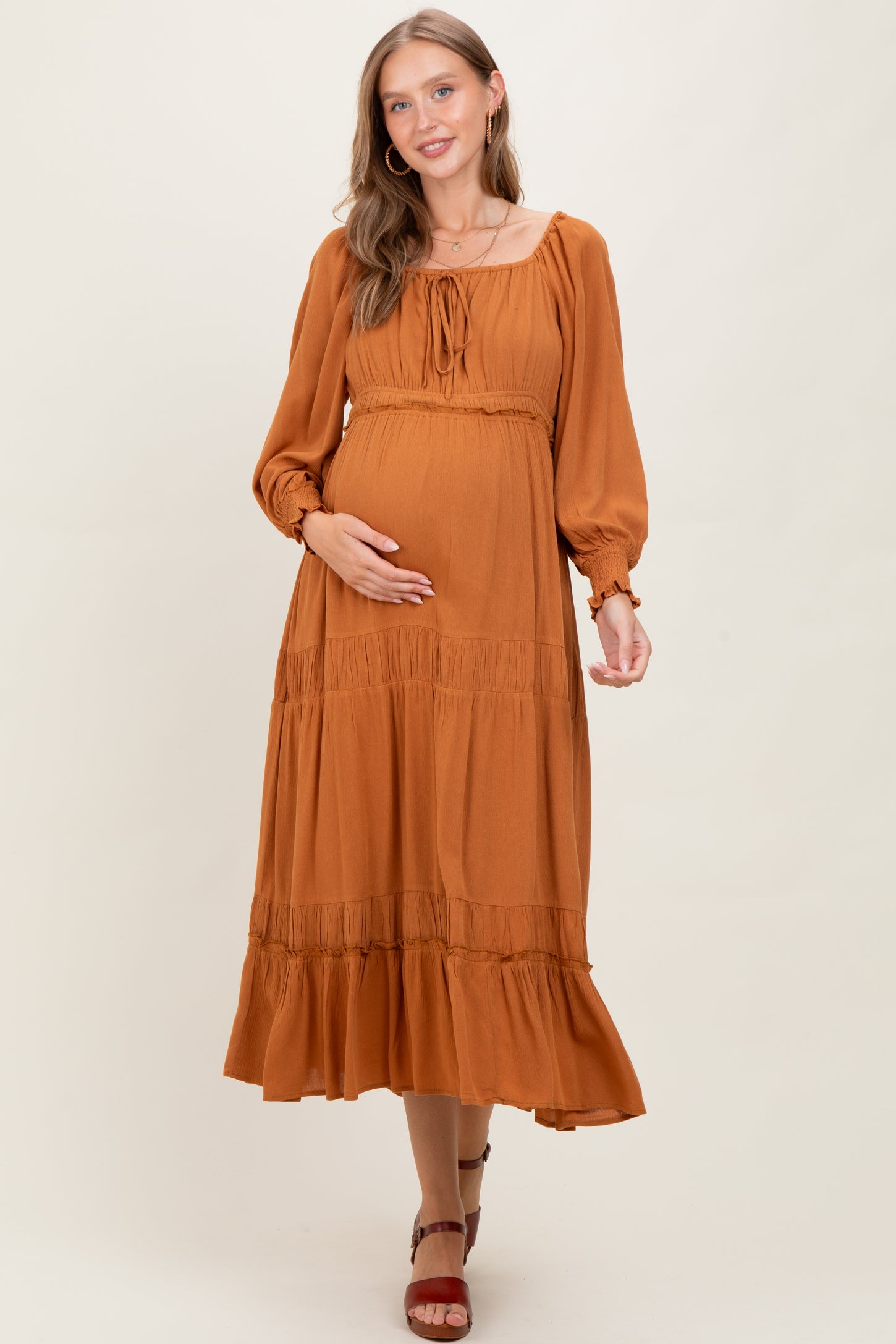 woman wearing a rust-colored long sleeve maternity dress with a tiered skirt and holding her baby bump