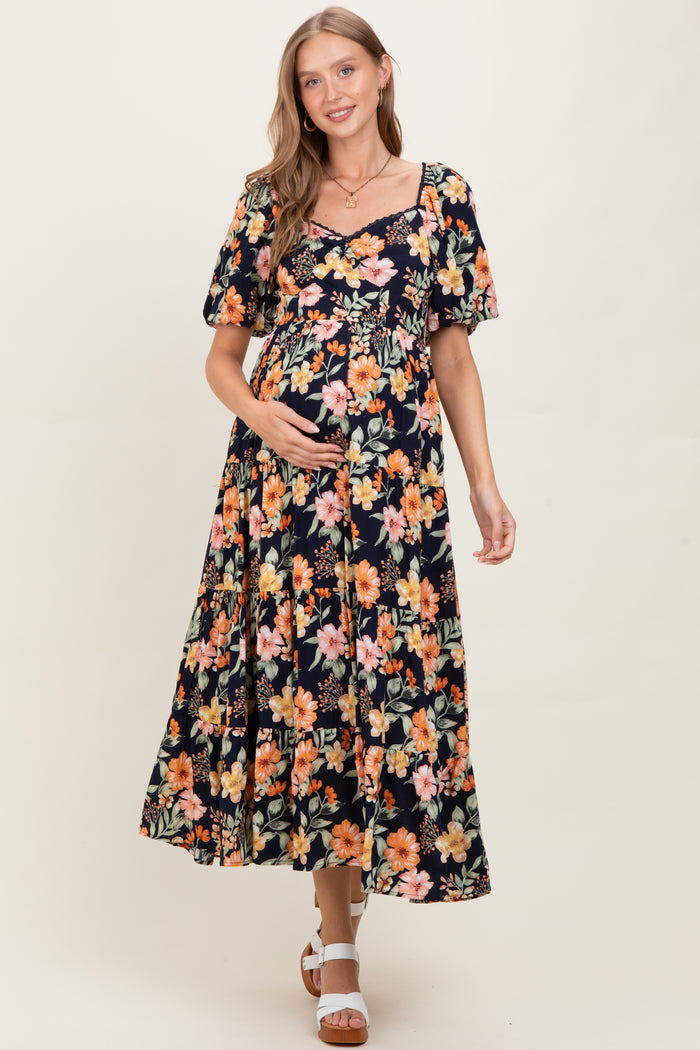 woman wearing a black maternity maxi dress with floral print and short puff sleeves, holding her baby bump