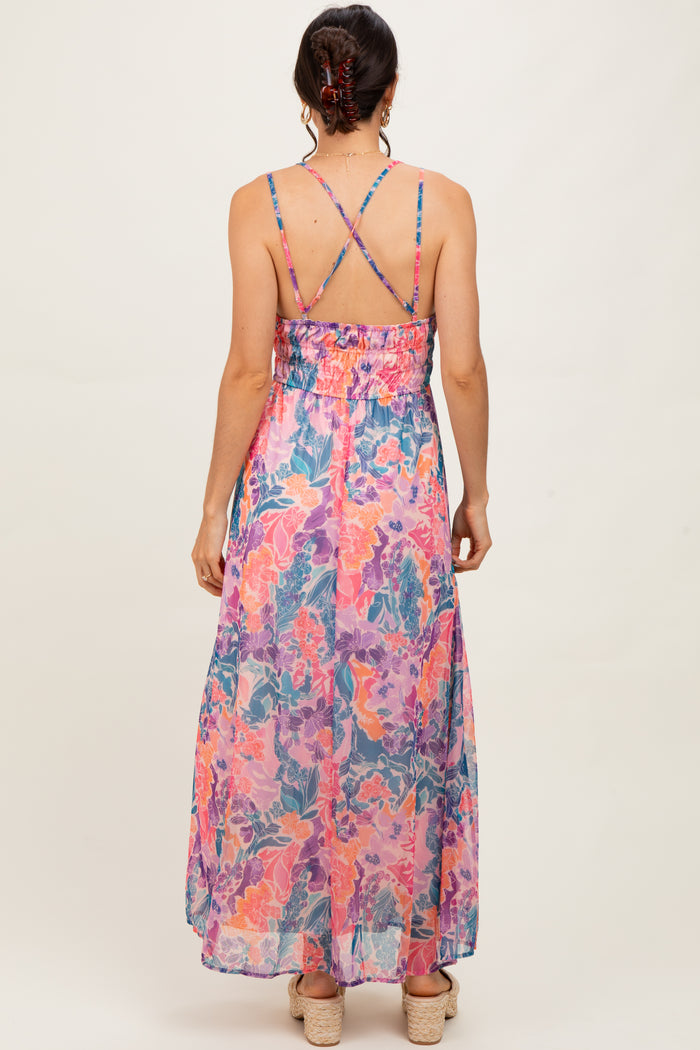 woman wearing a colorful floral maxi dress with crisscross straps and a smocked waist, seen from the back