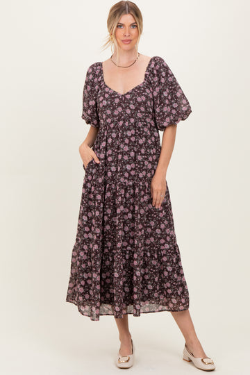 woman wearing a black floral maxi dress with puff sleeves and pockets, standing against a neutral backdrop
