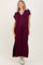 woman wearing a burgundy maxi dress with a collar and decorative trim, standing with a relaxed fit and side slits