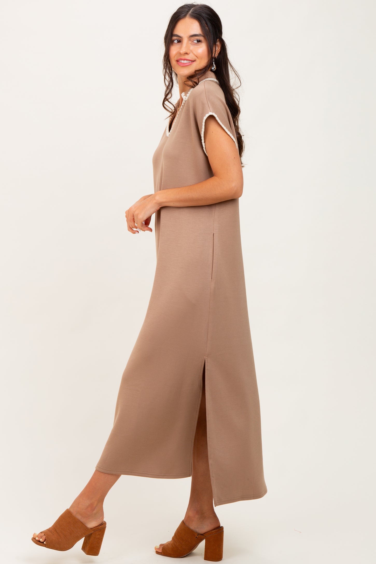 woman wearing a brown sleeveless maxi dress with side slits and a relaxed fit, standing sideways on a light background