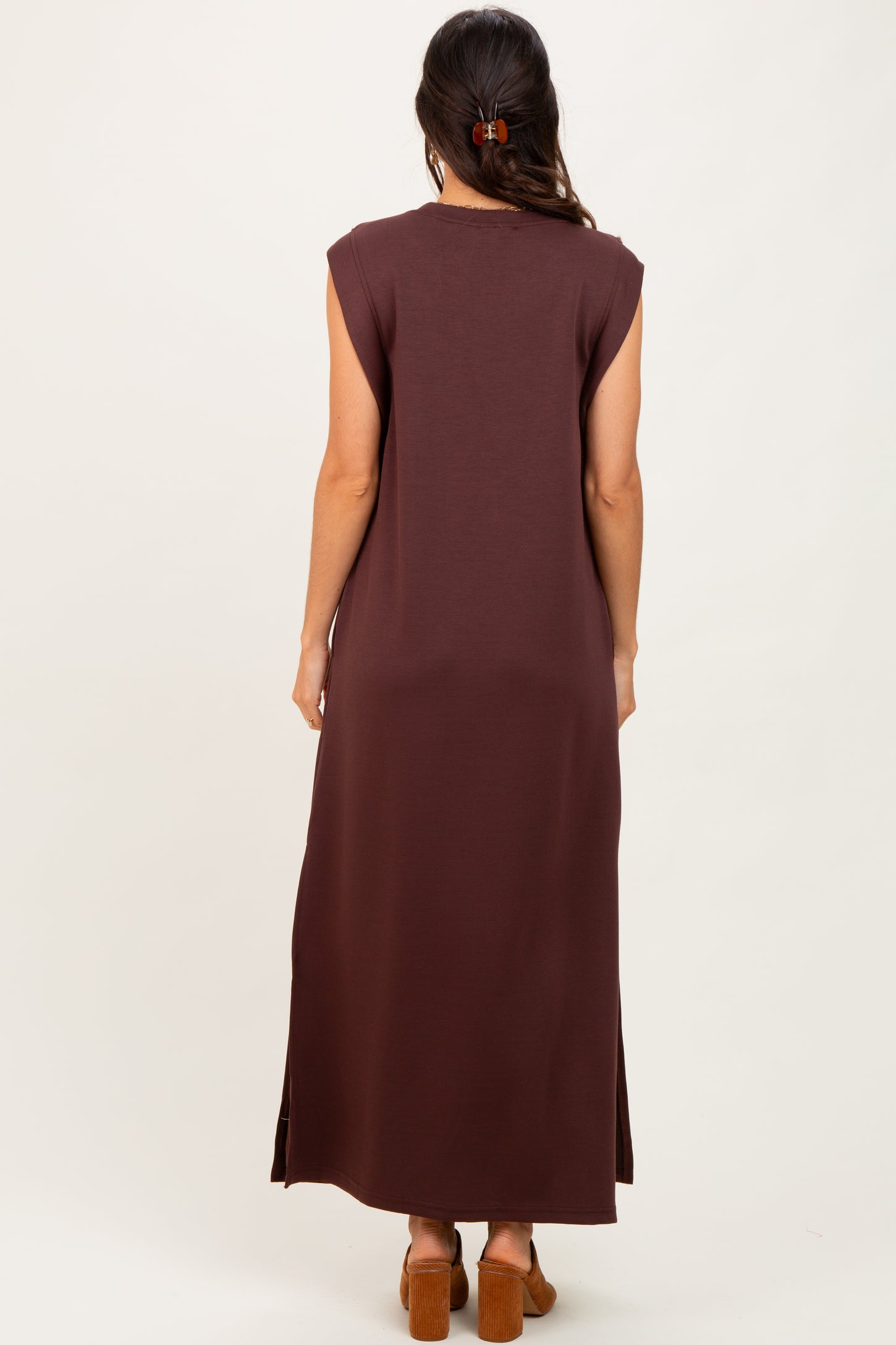 woman wearing a long brown sleeveless maxi dress with side slits, shown from the back