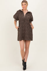 woman wearing a brown leopard print short dress with a zip-up collar and puff sleeves, standing with hands in pockets