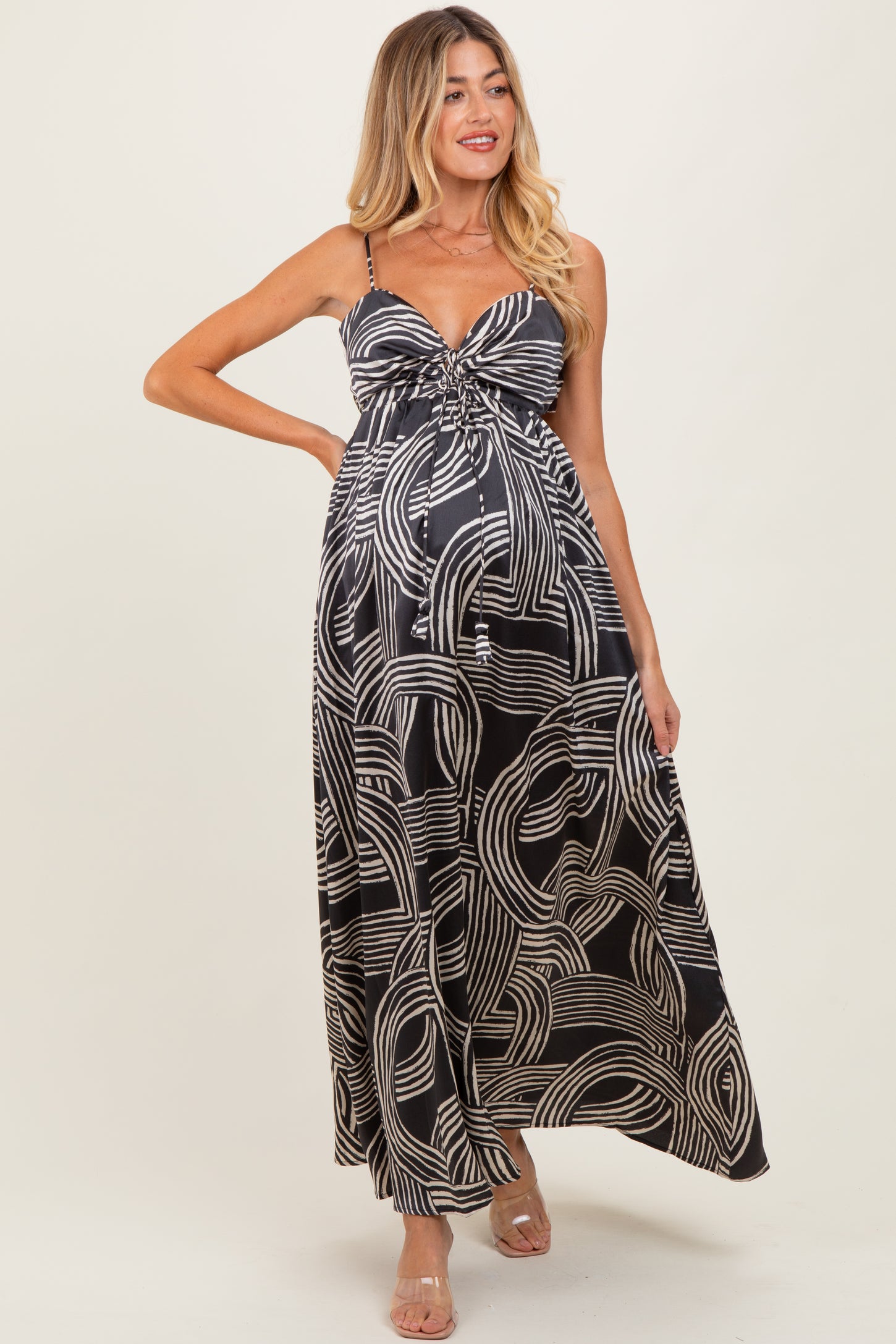 woman wearing a black and white patterned maternity maxi dress with a twist front and adjustable straps, showing her baby bump