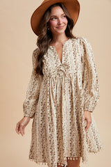 woman wearing a cream floral print long sleeve dress with a v-neck and pom pom hem, accessorized with a wide-brimmed hat