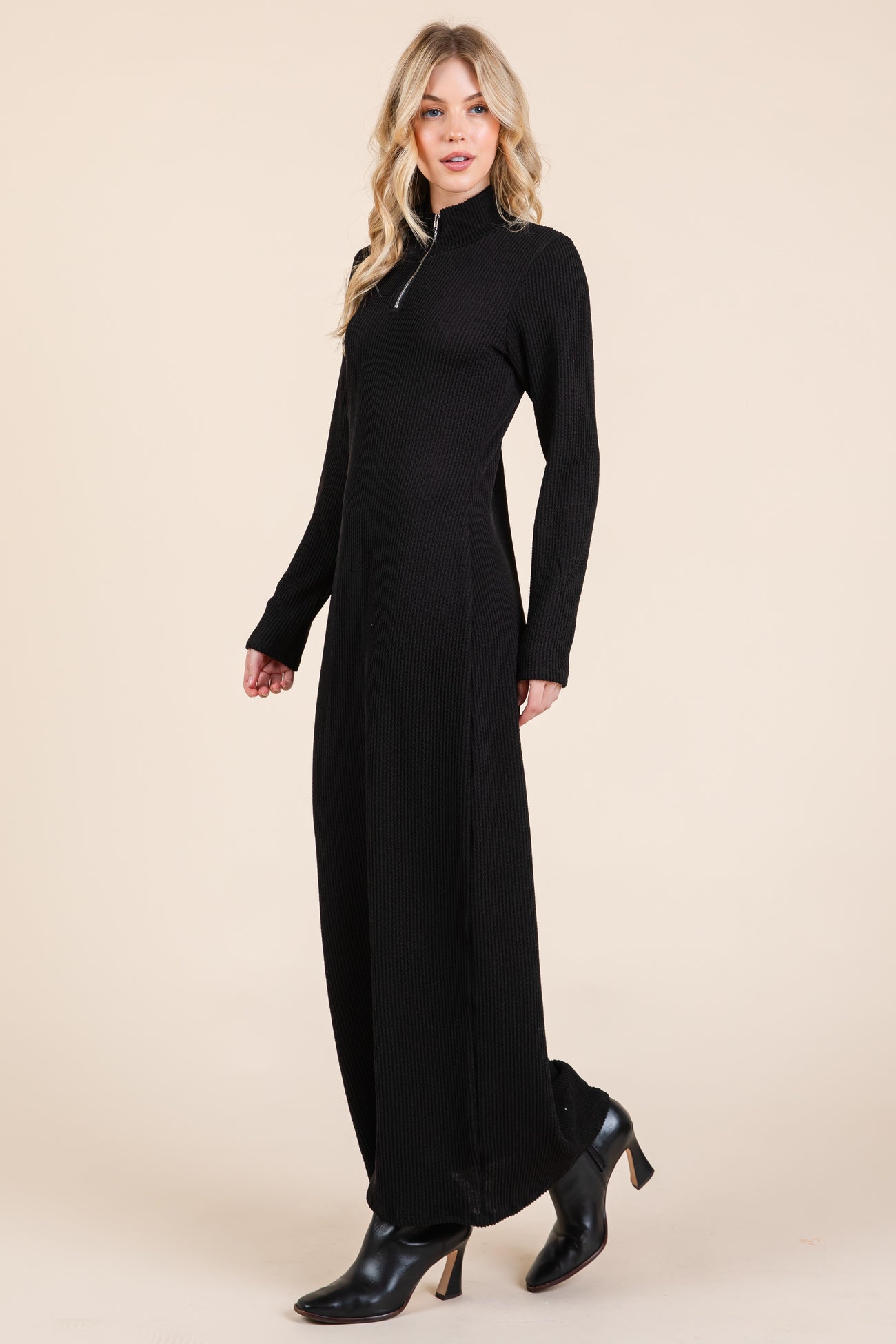 woman wearing a black long sleeve maxi dress with a stand collar and side slits paired with black heeled boots