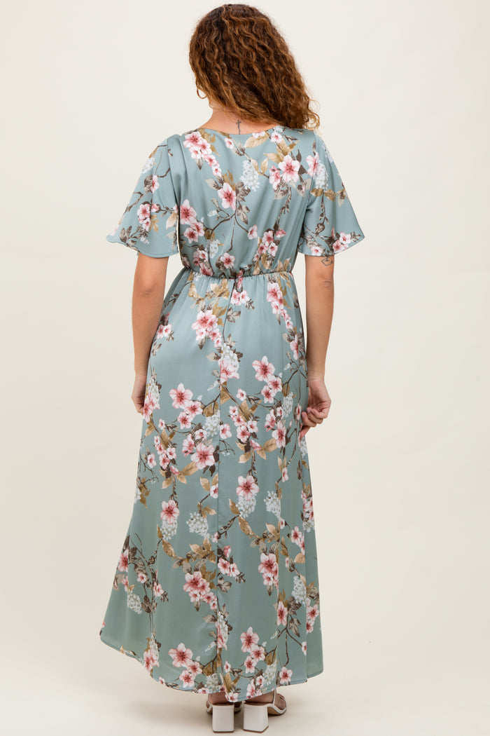 woman wearing a back view of a floral print maxi dress in teal with short flutter sleeves and a cinched waist