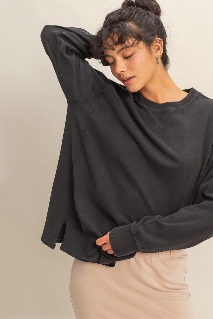 woman wearing a black oversized sweatshirt with dropped shoulders and side slits, paired with a beige skirt
