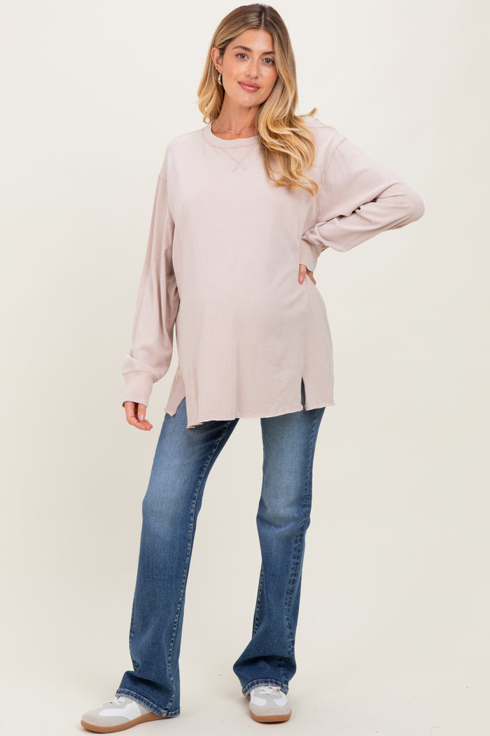 woman wearing a light pink maternity long sleeve top with side slits and blue bootcut jeans, showing her baby bump