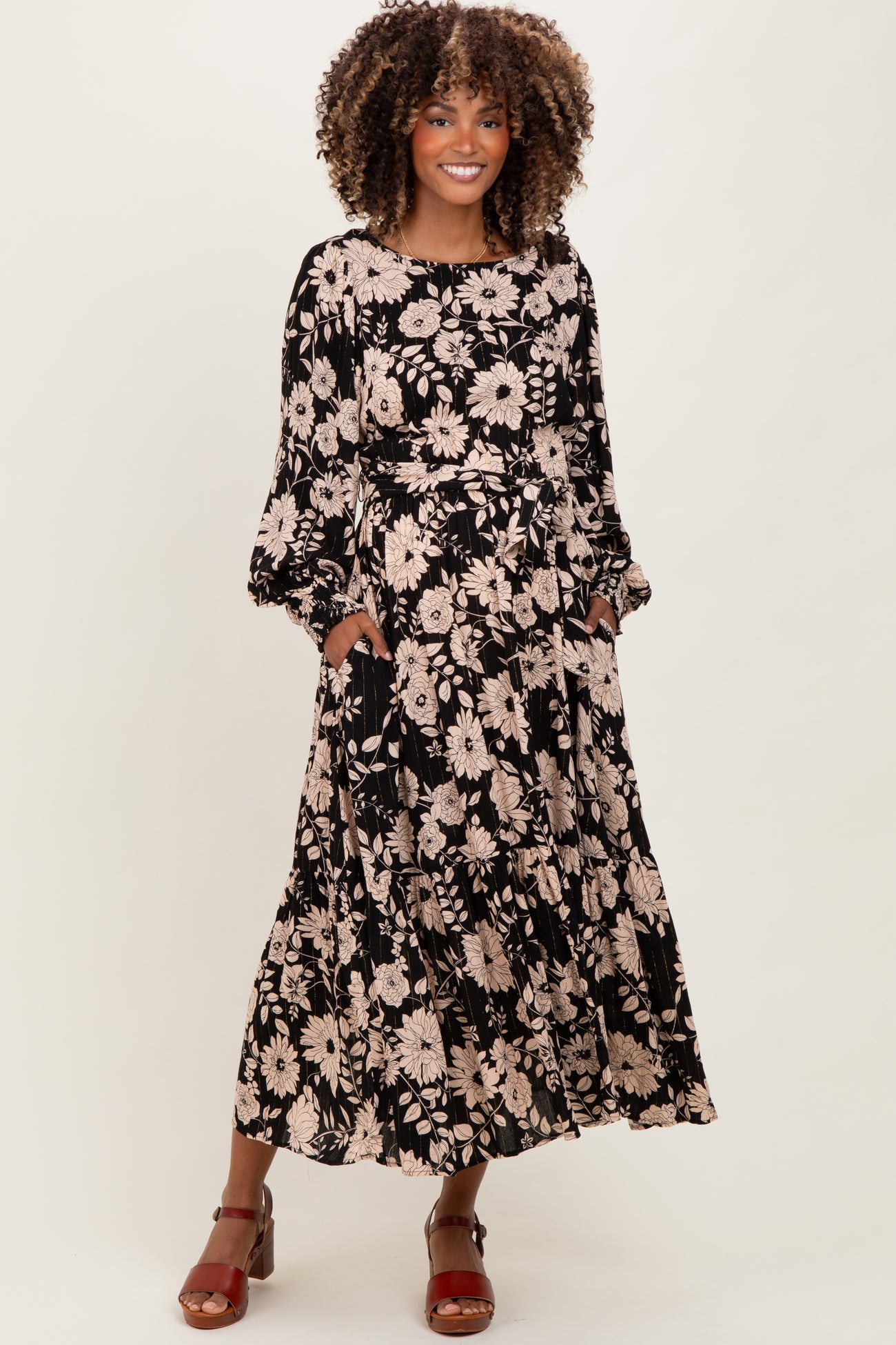 woman wearing a black floral maternity maxi dress with long sleeves and pockets, smiling while standing