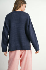 woman wearing a navy blue oversized textured sweater and pink striped wide-leg pants, viewed from the back
