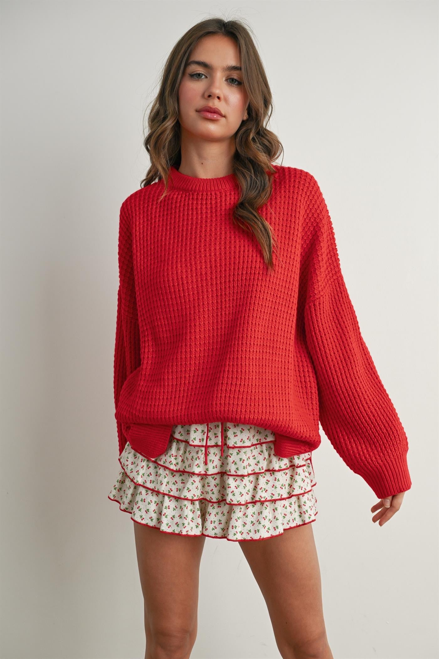 woman wearing a red oversized knitted sweater and a white floral ruffled skirt