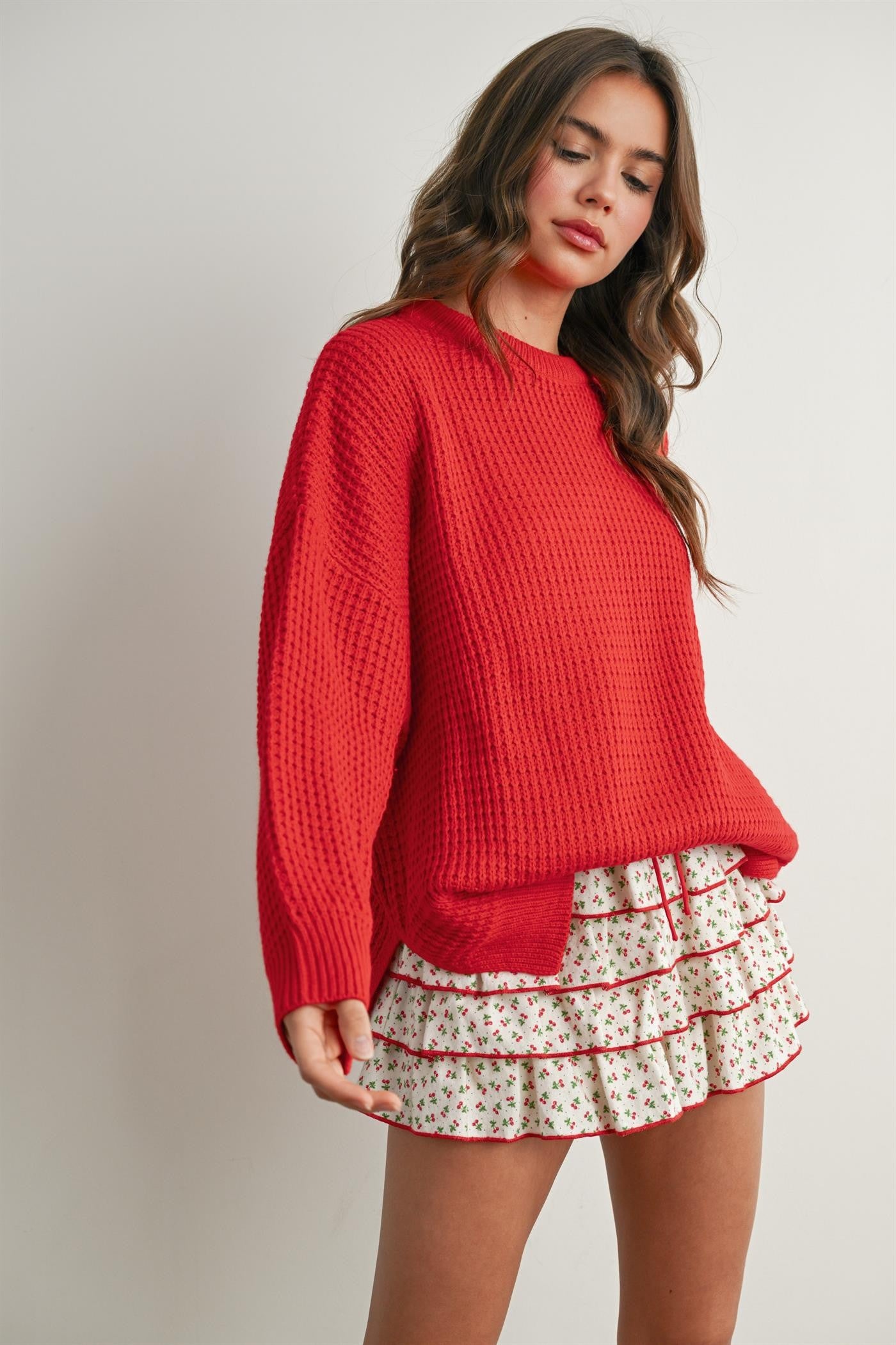 woman wearing a bright red oversized sweater with a textured finish and paired with a white floral ruffled mini skirt