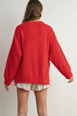 woman wearing a red oversized knit sweater with a textured pattern and white floral shorts, viewed from the back