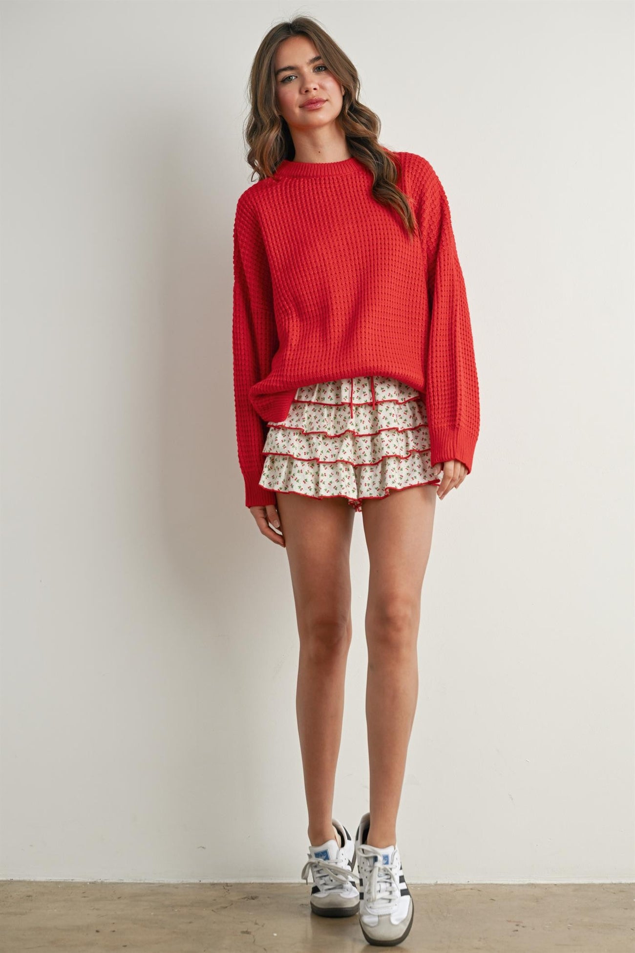 woman wearing a red oversized knit sweater and a floral tiered mini skirt with white sneakers