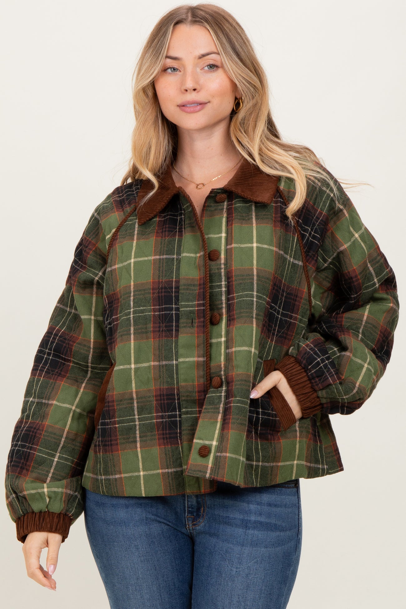 woman wearing a green and brown plaid quilted jacket with a collar and button front, styled with blue jeans