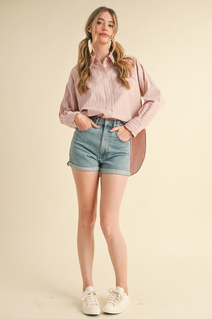 woman wearing a pink and white striped button-up shirt and high-waisted denim shorts with white sneakers