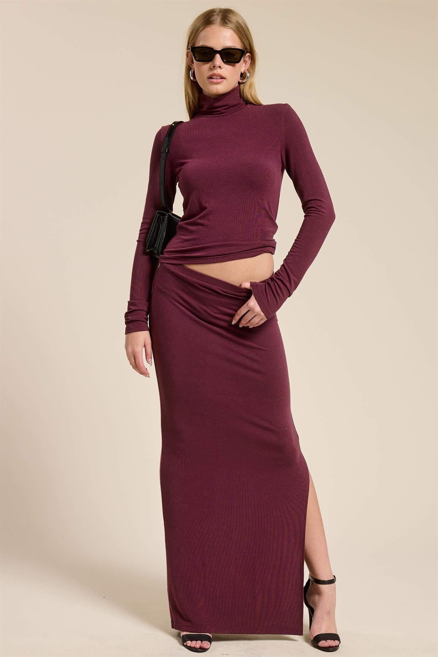 woman wearing a burgundy two-piece long sleeve top and high waist maxi skirt with a side slit and sunglasses