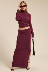 woman wearing a maroon two-piece set with a fitted turtleneck and a long skirt featuring a side slit