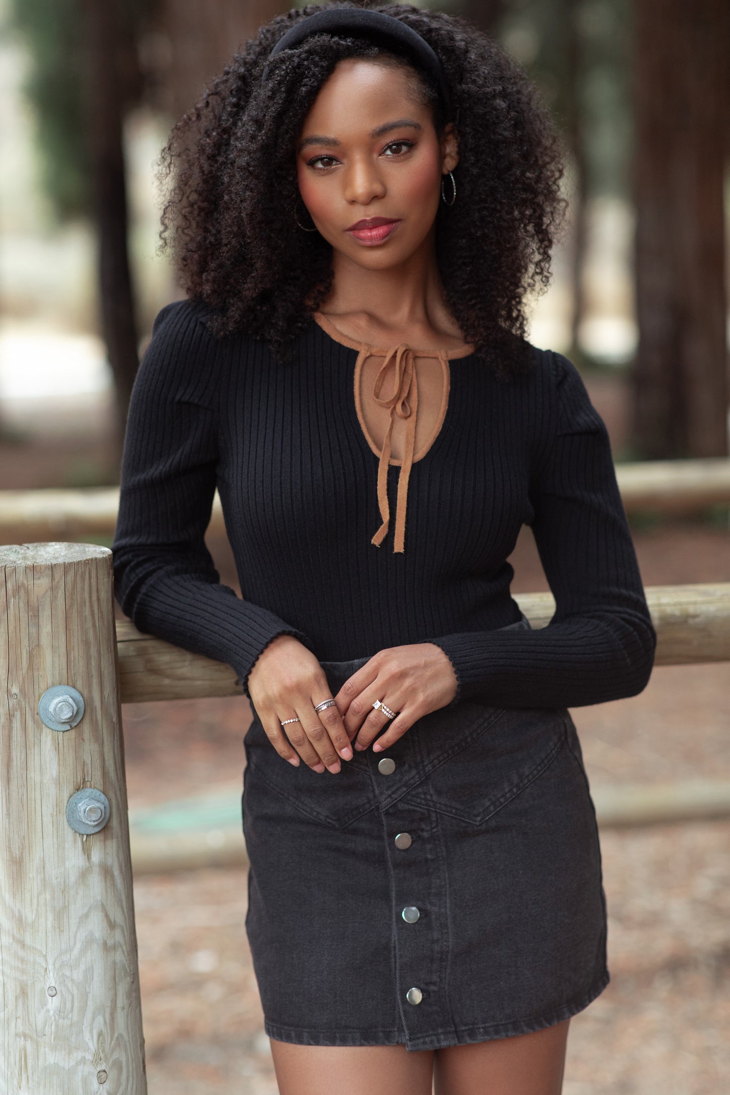 woman wearing a black ribbed long sleeve top with a tan neckline tie and a black denim mini skirt