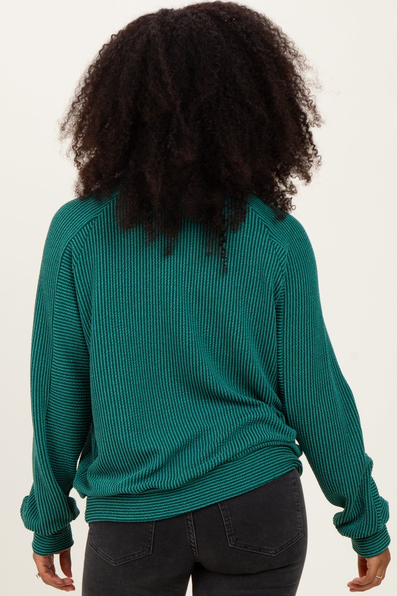 woman wearing a teal ribbed long sleeve sweater, viewed from the back, paired with black jeans