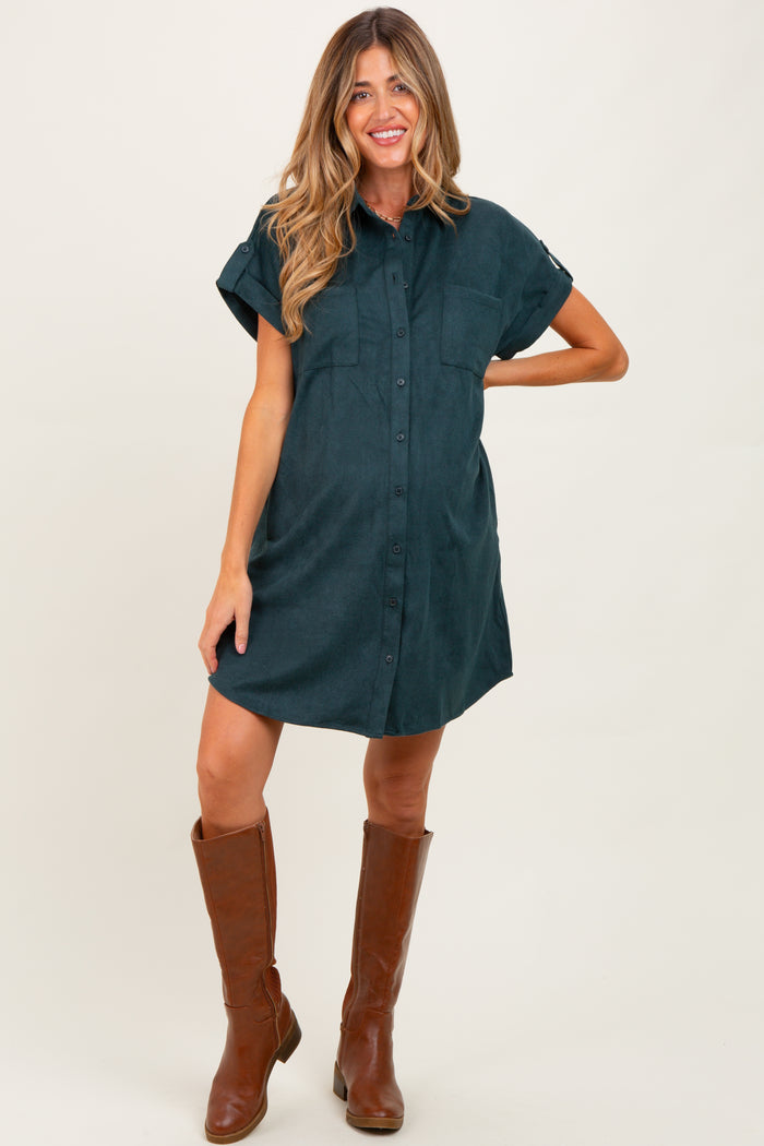 woman wearing a dark green maternity shirt dress with short sleeves and chest pockets, smiling while standing