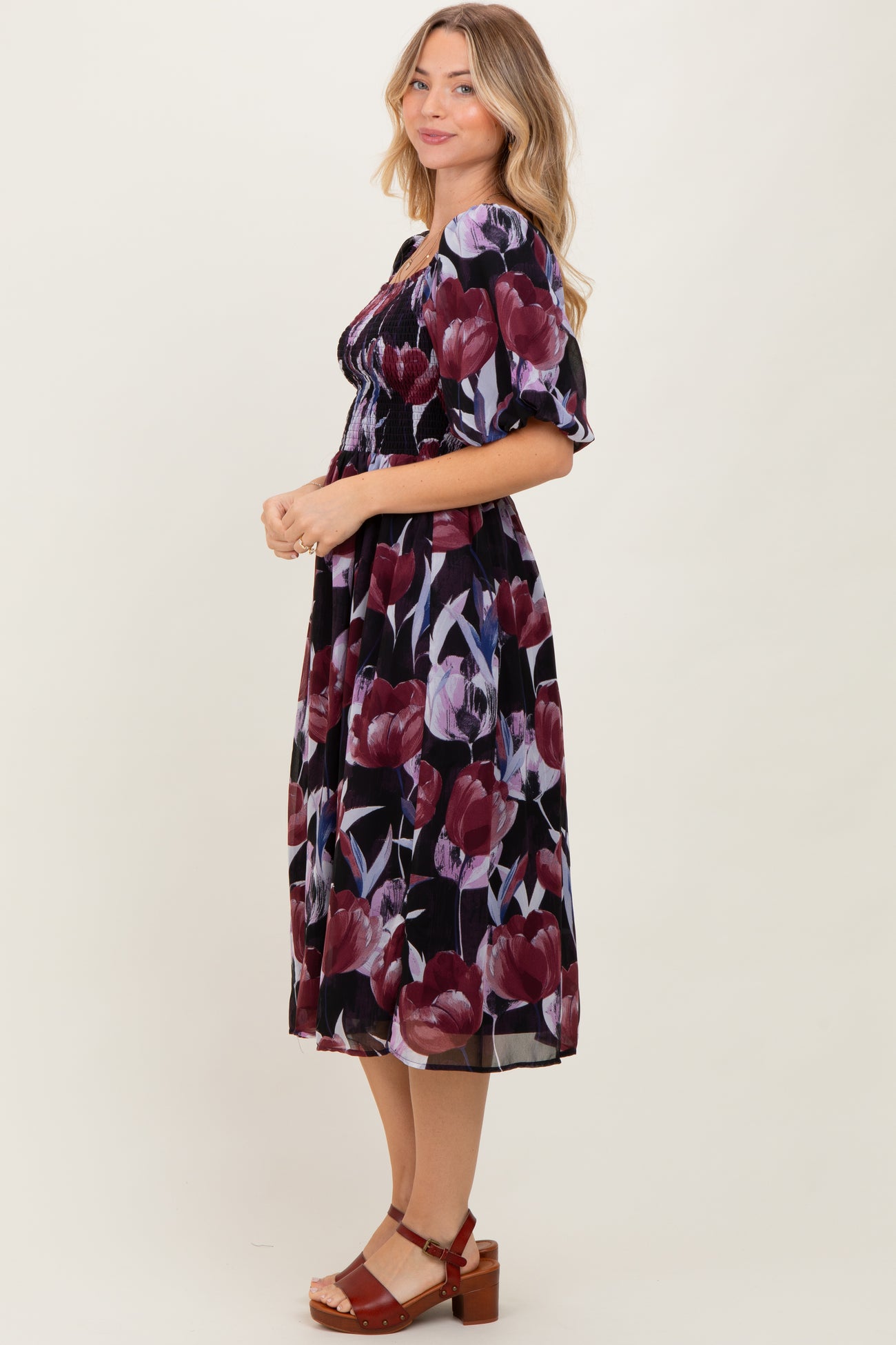 woman wearing a black floral midi dress with puff sleeves and a smocked waist, standing in profile