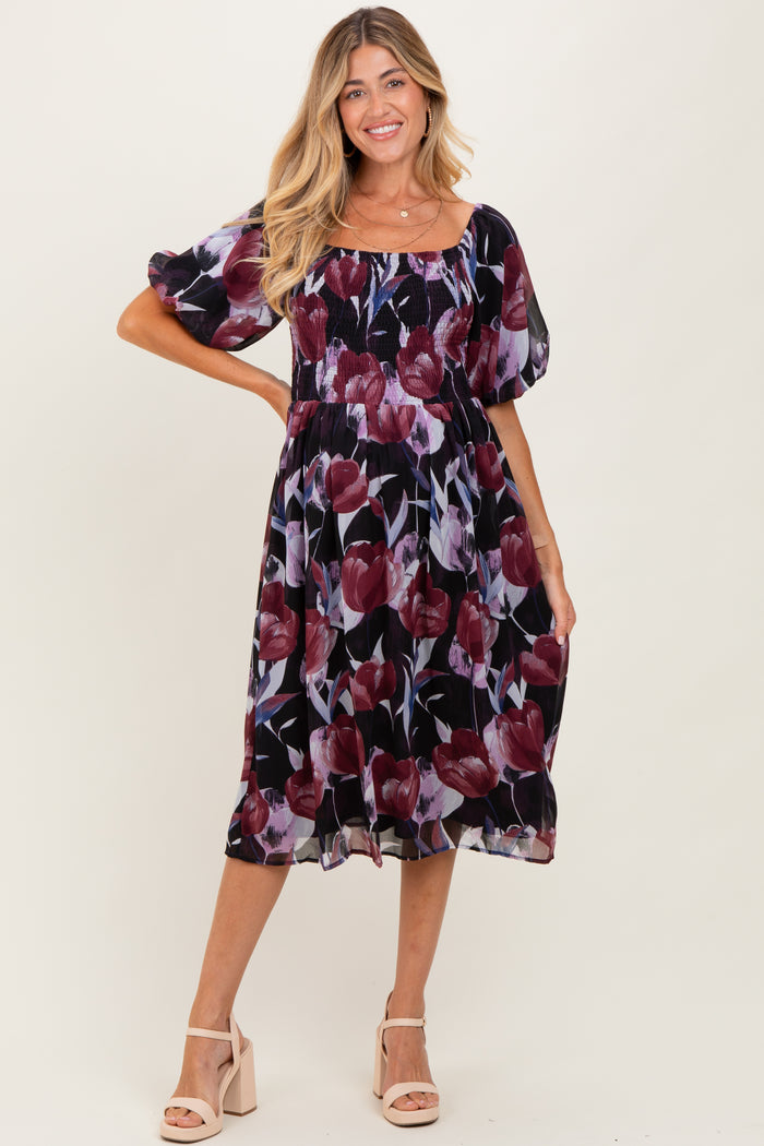 woman wearing a floral maternity dress with puff sleeves and a fitted bodice, posing and smiling