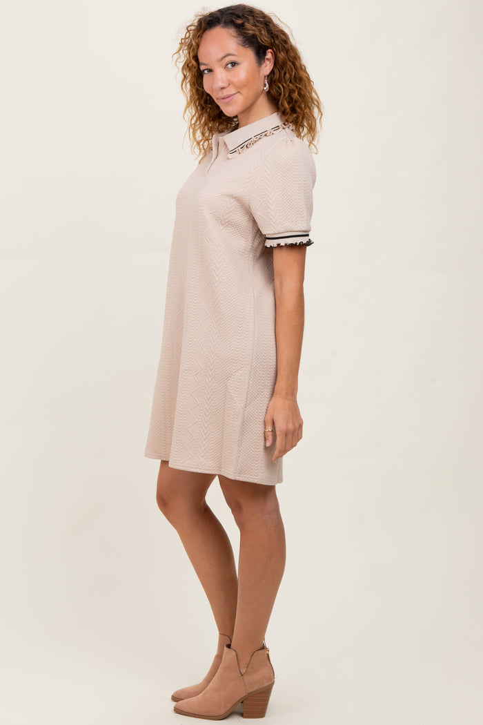 woman wearing a beige short sleeve dress with a textured pattern and decorative collar, styled with ankle boots