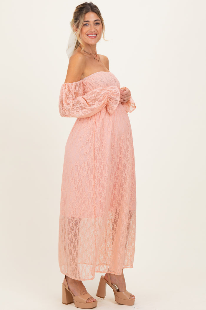 woman wearing a pink lace off-the-shoulder maternity dress and holding her baby bump