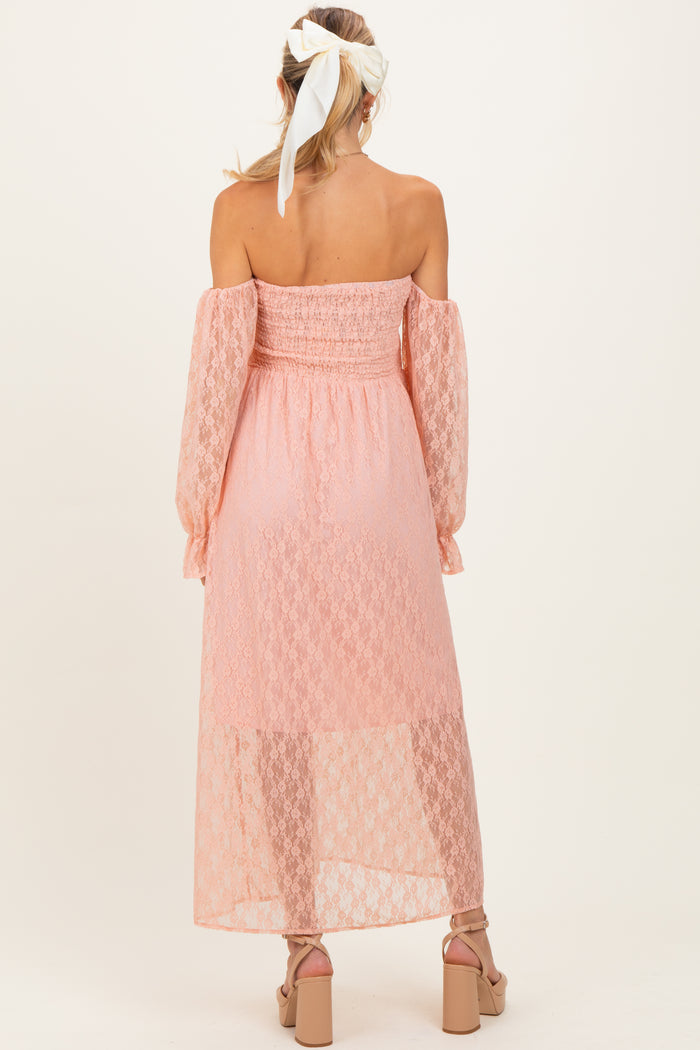 woman wearing a light pink off-shoulder maternity dress with long sleeves and a sheer overlay, showing no baby bump