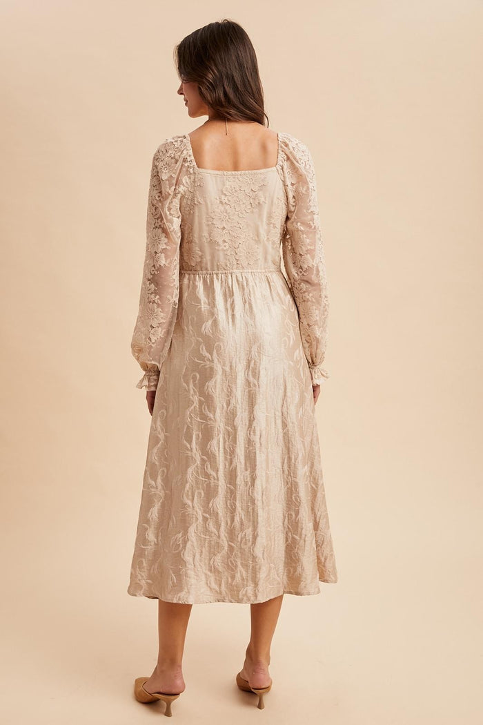 woman wearing a beige textured long sleeve dress with floral embroidery and a fitted waist, viewed from the back